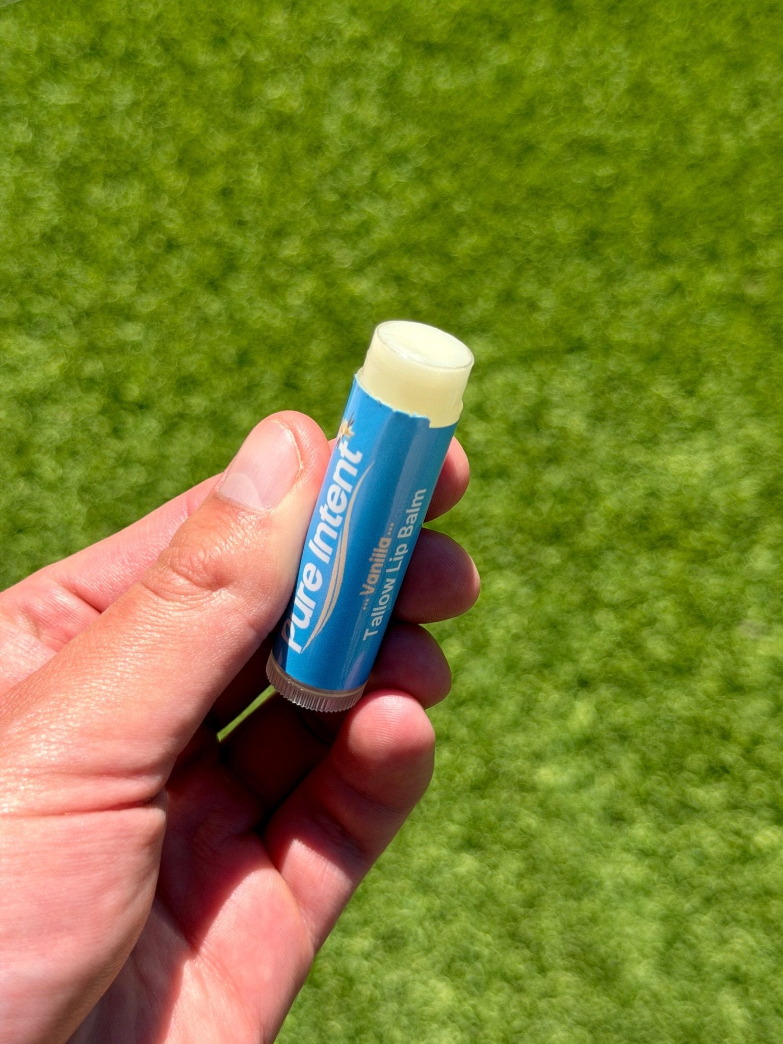 Hand holding a tube of Pure Intent lip balm against a green background