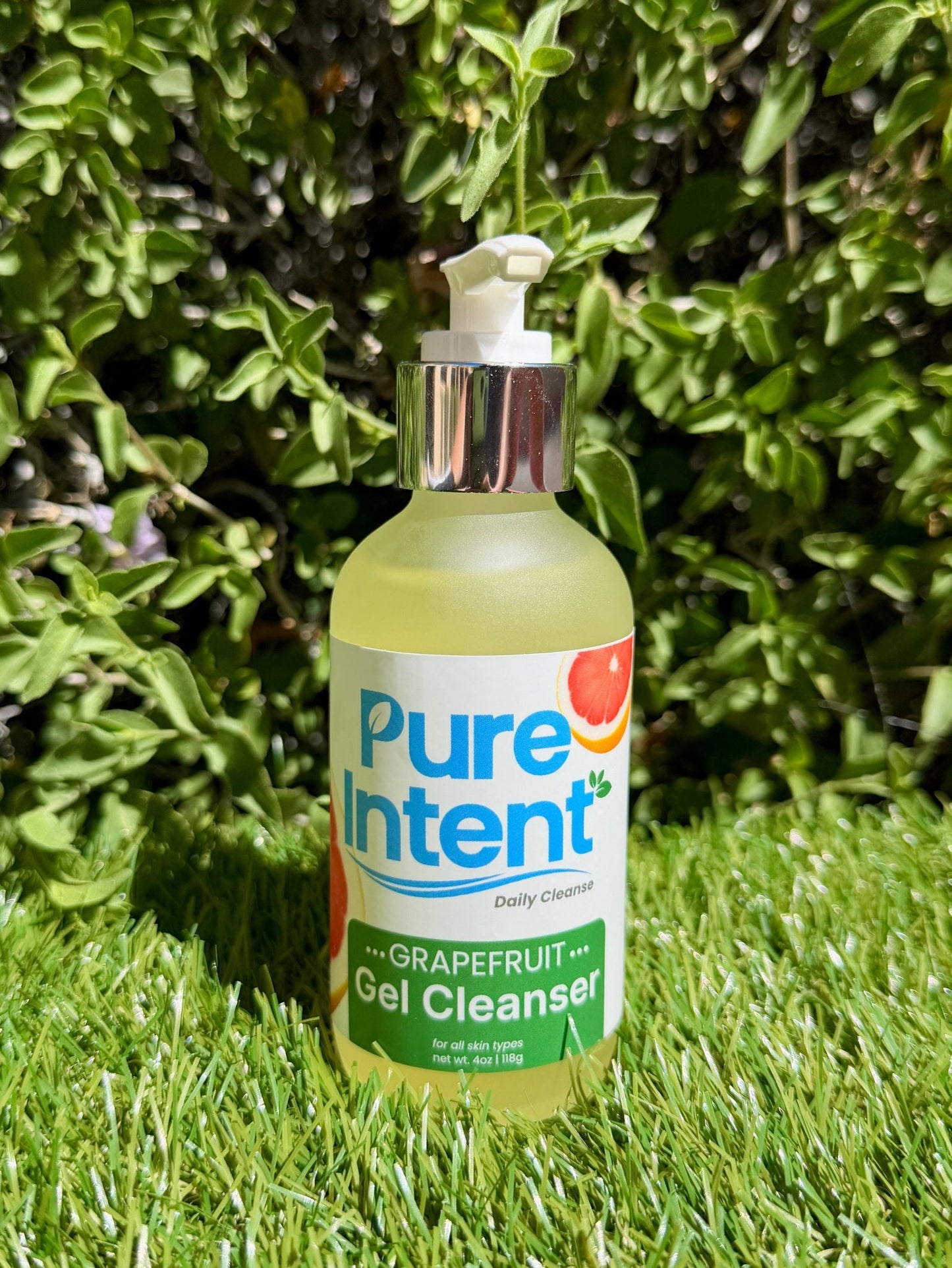 Bottle of Pure Intent Grapefruit Gel Cleanser on grass with greenery in the background