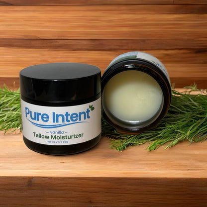 Pure Intent Tallow Balm jars displayed on a natural wood surface with greenery, highlighting organic skincare ingredients.